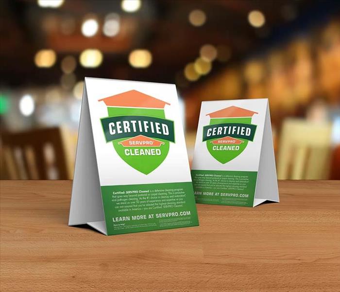 Table tent signs describing the Certified: SERVPRO Cleaned program on top of a wooden table.